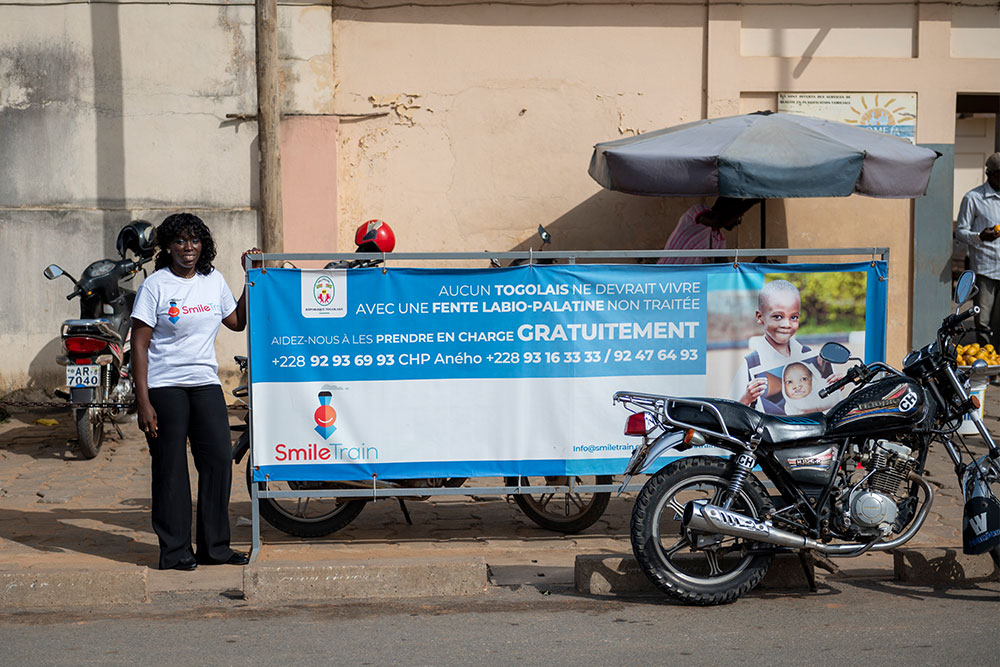 Dr. Nina Capo-Chichi steht lächelnd neben einem Smile Train-Schild in Togo